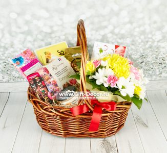 Gift basket with assorted chocolates and a colorful flower bouquet on a wooden surface, tied with a red ribbon
