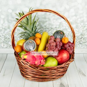 Basket of assorted fruits including pineapple, grapes, dragon fruit, apples, pears, bananas, and two jars of jam.